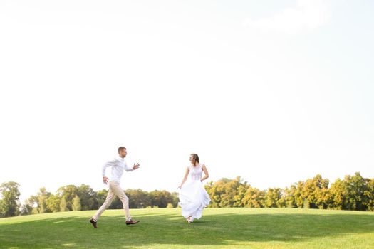 Groom and pretty bride running and playing on grass. Concept of wedding photo session on open air and nature.