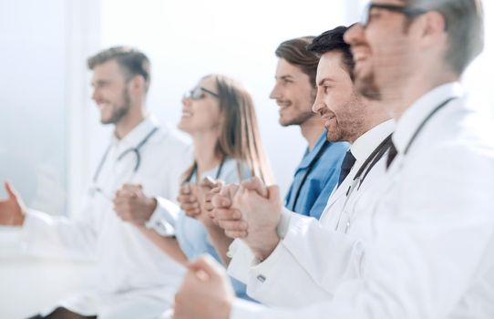 Happy group of people in white coats holding hands during a conference call.