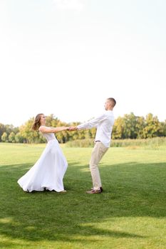 Happy european groom and bride dancing on grass. Concept of wedding photo session on open air and nature.