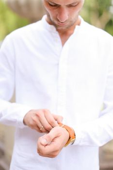 Caucasian happy groom looking at watch and waiting for bride outside. Concept of bridal photo session and young man.