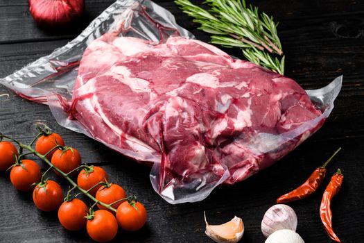 Fresh, raw, vacuum packed cut lamb meat set, with ingredients and herbs, on black wooden table background