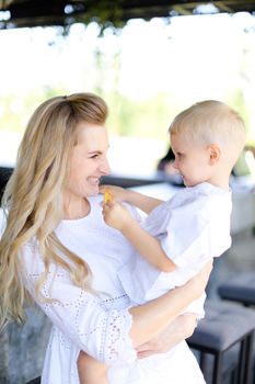 Young smiling mother holding baby outside and wearing white clothes. Concept of motherhood and child.