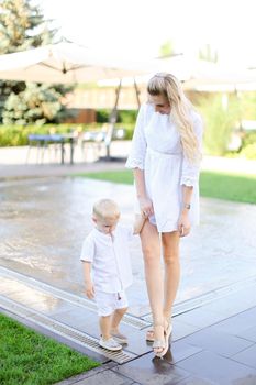 Young happy mother walking with little baby outside near fountain. Concept of walking in city and motherhood.