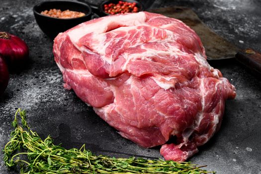 Raw pork neck meat piece for chop steak set, with ingredients and herbs, on black dark stone table background