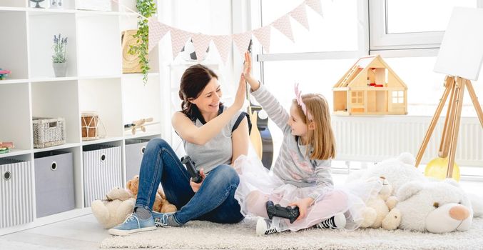 Cheerful daughter and mother giving high five in bright room