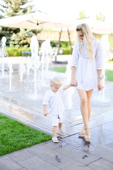 Young caucasian mother walking with little baby outside near fountain. Concept of walking in city and motherhood.