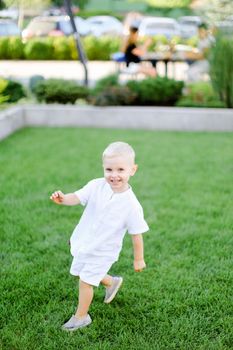 Little baby standing on grass and wearing white clothes. Concept of childhood and summer.