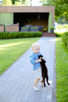 Little boy in jeans shirt standing with cat in yard. Concept of kids, childhood and pets.