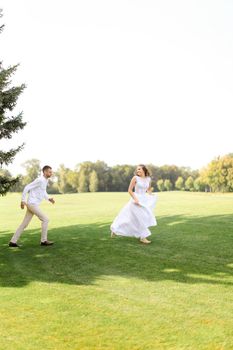 Groom and caucasian bride running and playing on grass. Concept of wedding photo session on open air and nature.