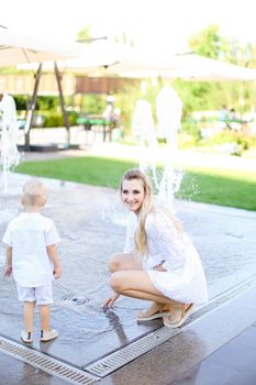 Young happy mother playing with little baby outside near fountain. Concept of walking in city and motherhood.