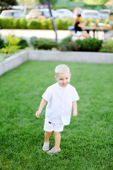 Little child standing on grass and wearing white clothes. Concept of childhood and summer.