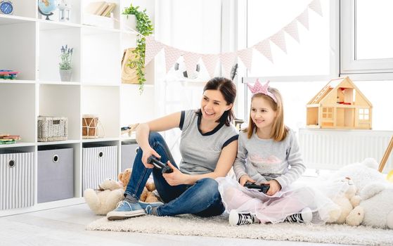 Happy mother and daughter playing video game in children room