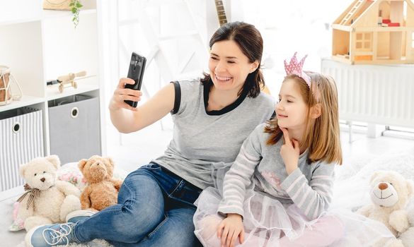 Smiling mother with daughter taking selfie in cute kids room