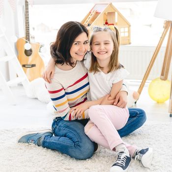Smiling woman with little girl sitting on floor at home