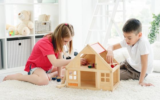 Cute little boy and girl playing with wooden doll house indoors