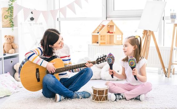 Beautiful woman playing guitar and singing with cute little girl