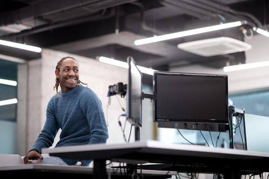 Portrait of young smiling african american male software developer sitting on office desk at modern startup office