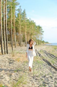 Young female person walking on sand beach and wearing white clothes. Concept of summer vacations.