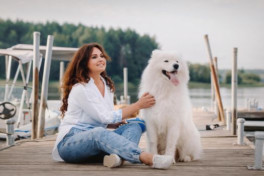 a happy woman with a big white dog lies on a pier near the sea at sunset.