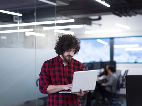 young smiling successful male software developer using laptop computer while standing at modern startup office