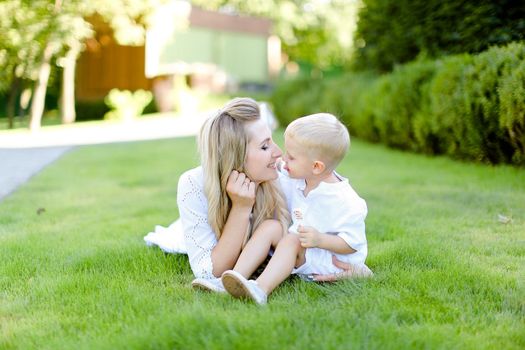 Young mother sitting with little child on grass in yard. Concept of motherhood and summer vacations.