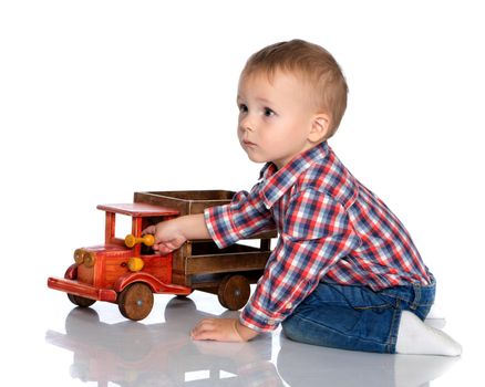 Cute little boy is playing with a toy wooden car on a white background in the studio. The concept of a happy childhood, learning and education in the family. Isolated.