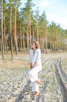 Blonde girl walking on sand beach and wearing white clothes. Concept of summer vacations.