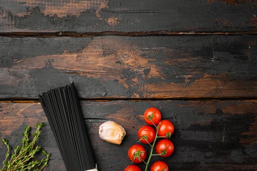 Uncooked black spaghetti and the ingredients set, on old dark wooden table background, top view flat lay, with copy space for text