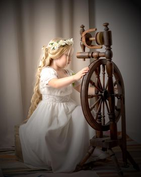 A cute little girl wove a wool with a rotating wheel. Retro style, memories of the past.