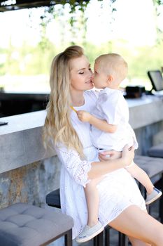 Young mother holding baby outside and wearing white clothes. Concept of motherhood and child.