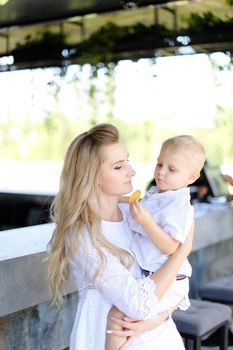 Young caucasian mother holding baby outside and wearing white clothes. Concept of motherhood and child.