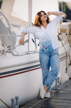 a happy woman with long hair stands on the pier near the yacht.