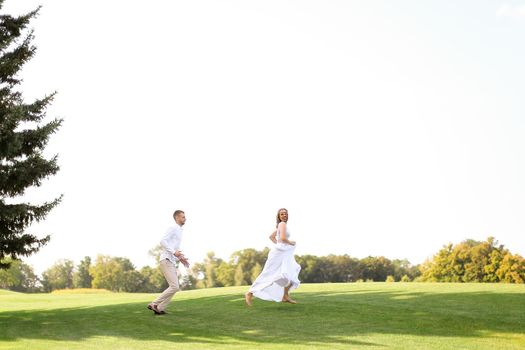 Groom and bride running and playing on grass. Concept of wedding photo session on open air and nature.