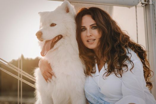 a happy woman with a big white dog on a white yacht in the sea.