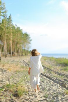 Back view of girl walking on sand beach and wearing white clothes. Concept of summer vacations.