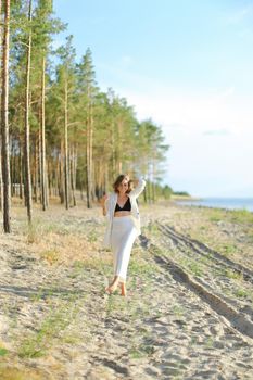 Woman walking on sand beach and wearing white clothes. Concept of summer vacations.