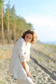 Nice young female person walking on sand beach and wearing white clothes. Concept of summer vacations.