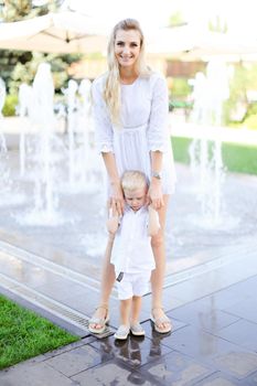 Young smiling mother walking with little baby outside near fountain. Concept of walking in city and motherhood.