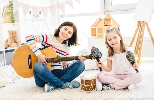 Nice little girl and mother playing musical instruments in kids room