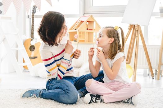 Pretty mother and daughter playing with stick lips and glasses