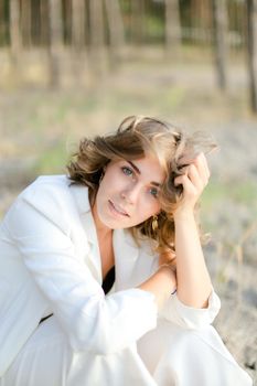 Young сaucasian girl sitting on sand beach and wearing white clothes.