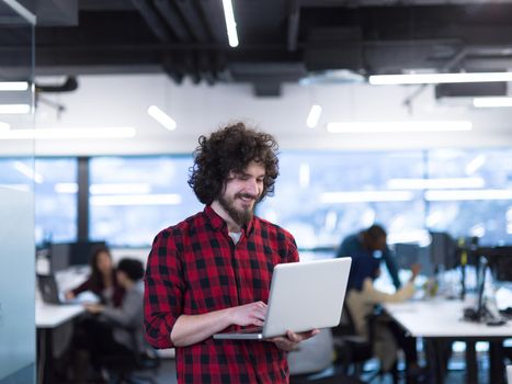 young smiling successful male software developer using laptop computer while standing at modern startup office