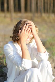 Young smiling girl sitting on sand beach and wearing white clothes.