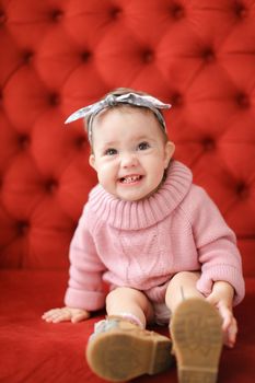 Little funny female baby sitting in red background on sofa. Concept of babias and photo session.