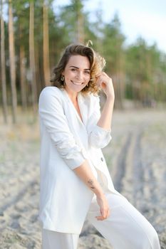 Blonde smiling girl in white clothes walking on sand beach and wearing white clothes. Concept of summer vacations.