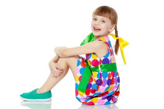 A beautiful Caucasian little blonde girl with long pigtails, in which large colored bows are braided, and a short bangs on her head. In a short summer dress, a pattern of multi-colored circles.