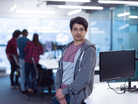 Portrait of young smiling successful male software developer standing at modern startup office