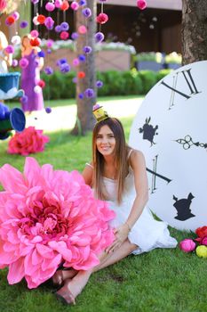 Young girl sitting at decorated place for children near big pink flower. Concept of beauty and festive decorations.