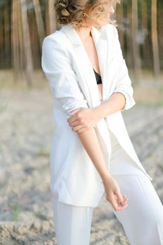 Blonde pretty girl in white clothes walking on sand beach and wearing white clothes. Concept of summer vacations.