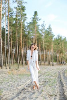 Blonde girl standing on sand beach and wearing white clothes. Concept of summer vacations.